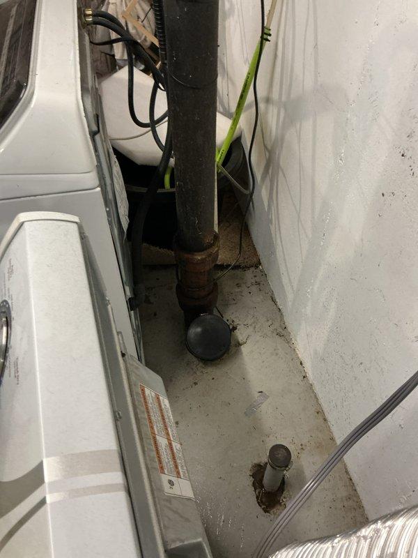 Responded to emergency main floor drain backup causing complete loss of water usage throughout residence due to basement flooding. Upon arrival, located floor drain in basement utility area adjacent to laundry appliances. Inspection revealed severely corroded drain pipe opening with extensive rust deterioration and compromised pipe integrity. The circular drain opening showed significant metal oxidation with exposed deteriorated insulation material around the interior rim. Flexible metal conduit connection displayed signs of age and moisture exposure. Documented existing conditions showing concrete floor discoloration, dirt accumulation around drain area, and corroded metal fittings at pipe base. The 1960s-era stick-built home's original plumbing infrastructure exhibited advanced corrosion consistent with decades of use and moisture exposure. Photographed drain access point and surrounding utility space for record purposes. Assessed drainage system to determine source of backup and flo