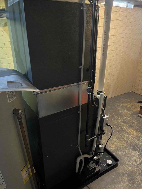 Completed installation of EnviroMaster Elite Series vertical HVAC furnace unit in residential utility room. Installed condensate drain system with PVC piping and condensate pump at base of unit, ensuring proper drainage functionality. Configured white PVC intake and exhaust venting system per manufacturer specifications, mounted electronic sensor/control device, and verified all electrical connections for safe operation.