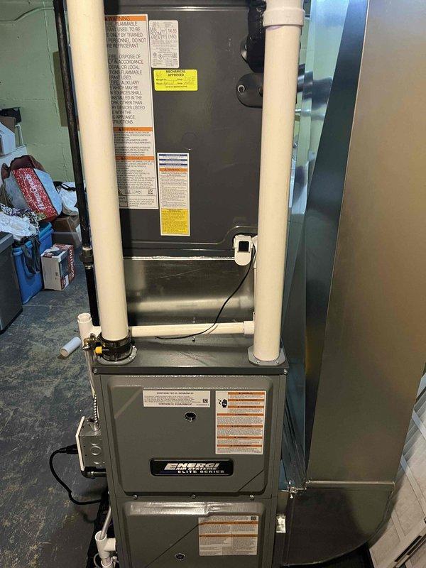 Completed installation of EnviroMaster Elite Series vertical HVAC furnace unit in residential utility room. Installed condensate drain system with PVC piping and condensate pump at base of unit, ensuring proper drainage functionality. Configured white PVC intake and exhaust venting system per manufacturer specifications, mounted electronic sensor/control device, and verified all electrical connections for safe operation.