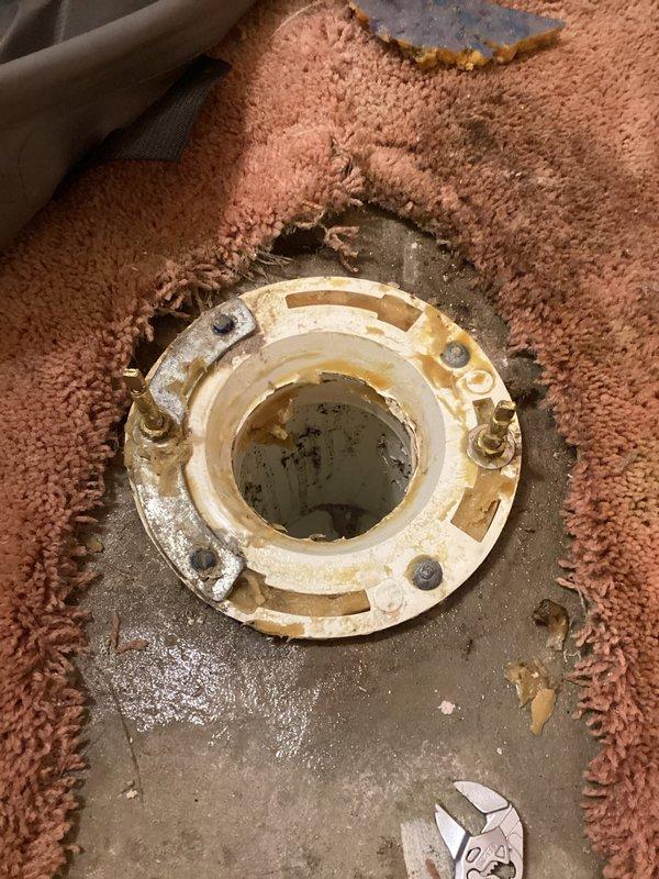 Responded to service call for loose toilet that was moving when sat upon. Upon inspection, found toilet flange bolts had loosened, causing instability in the fixture. Removed toilet to access flange assembly and assessed the installation. Tightened flange bolts securely to the concrete subfloor, ensuring proper anchoring. Inspected wax ring seal and flange condition for any damage or deterioration. Reset toilet onto flange with proper alignment, secured closet bolts, and torqued nuts evenly to manufacturer specifications to eliminate movement. Tested stability by applying pressure to confirm secure installation. Documented existing water damage staining on concrete subfloor and worn carpet condition around flange area for client's awareness.
