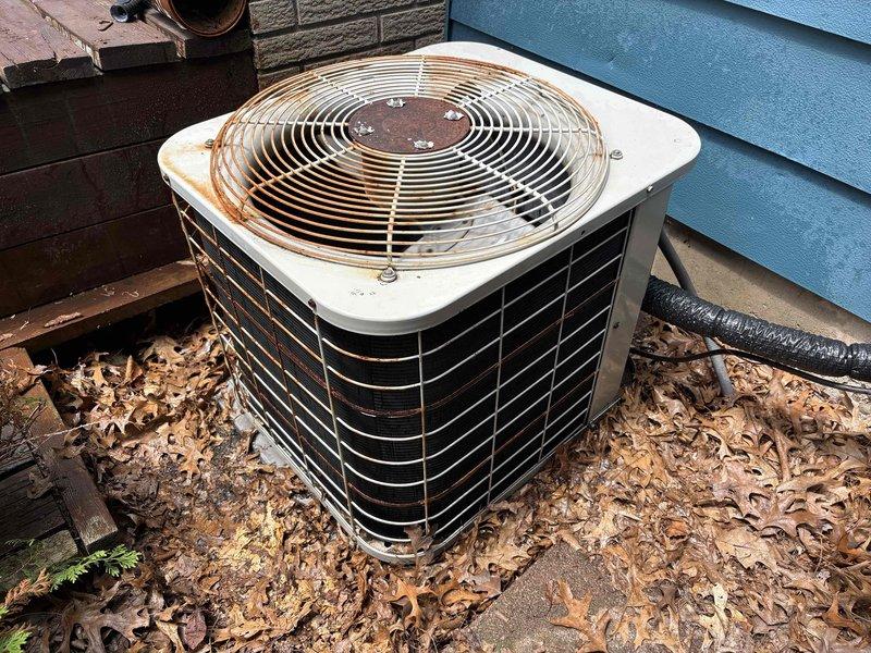 # NC-No Cool Service Call

Responded to no cooling complaint on 10-12 year old Carrier system with no power to outdoor unit. Upon arrival, found condenser unit showing significant age-related deterioration with heavy rust on top panel and cabinet. Unit located against building exterior with substantial leaf debris accumulation around base and on concrete pad. Performed visual inspection of outdoor equipment and documented existing conditions with photos showing weathered cabinet, corroded components, and environmental debris buildup affecting unit. System required further diagnostic evaluation to determine cause of complete power loss and assess viability of repairs given advanced age and deteriorated condition of equipment.