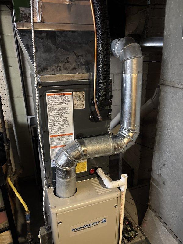 Completed full air conditioning system installation including outdoor condensing unit and indoor evaporator coil integration with existing forced-air furnace. Installed Trane brand condensing unit on concrete pad adjacent to home exterior, positioned near existing landscaping with proper clearances maintained. Ran refrigerant line set and electrical connections from outdoor unit through exterior wall penetration to basement mechanical room. Integrated new evaporator coil with existing furnace plenum and ductwork system. Installed condensate drain line with proper pitch and termination. Connected and secured all refrigerant lines with appropriate insulation. Completed electrical wiring to outdoor disconnect and indoor air handler connections. Evacuated refrigerant lines to manufacturer specifications, pressure tested system for leaks, and charged unit with proper refrigerant type and quantity. Verified proper airflow across evaporator coil and confirmed compatibility with existing April