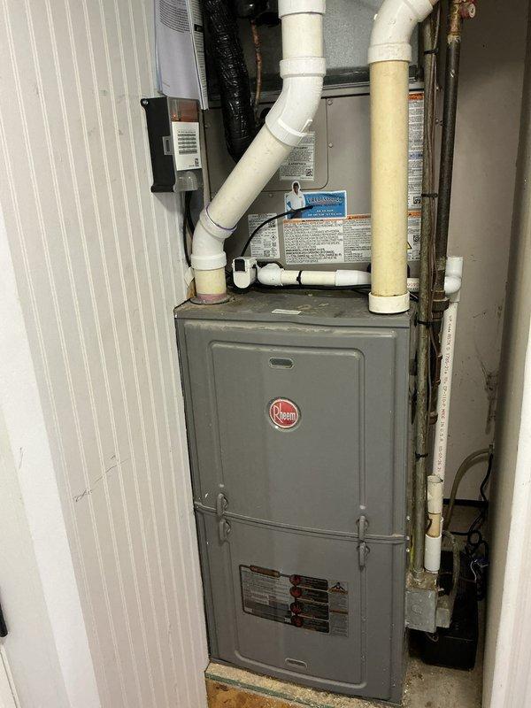 Completed full residential air conditioning system replacement in utility closet. Installed new Rheem furnace unit with integrated cooling coil, configured PVC condensate drainage and venting system with multiple elbows and joints for proper exhaust routing. Mounted electronic control components and connected black flexible supply ductwork. Ran and terminated refrigerant lines with copper piping, installed shut-off valves, and completed all electrical connections including wall-mounted receptacle. Secured all conduit runs along walls and ceiling with appropriate mounting brackets. System tested and verified operational upon completion.