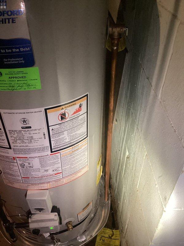 Responded to water leak alarm triggered by water accumulation in drain pan beneath Bradford White water heater. Upon inspection, confirmed approximately 1-year-old Bradford White WT 04 unit with water present in safety pan. Examined all visible plumbing connections, copper supply lines, and tank exterior for signs of active leakage or seepage. Documented equipment condition and installation with photographs showing unit positioning, manufacturer labels, plumbing connections, and surrounding utility space conditions. Verified drain pan alarm functionality and monitored for continued water accumulation to determine leak source.