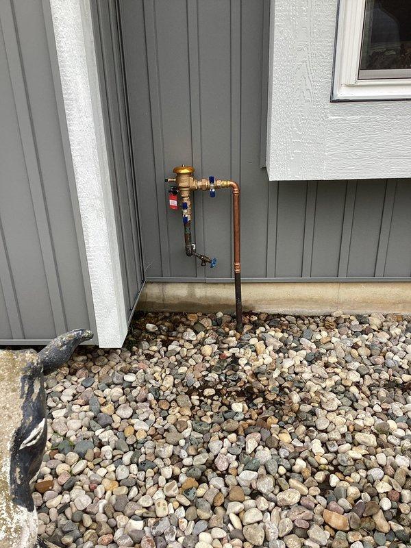 Responded to plumbing leak in backflow prevention system mounted on exterior wall. Upon inspection, identified active leak at brass backflow preventer assembly with multiple ball valves and copper piping connections. Assessed the outdoor plumbing installation which showed signs of weathering and exposure to elements. Repaired leak by tightening compromised fittings and replacing worn components as needed. Tested all blue-handled ball valves for proper operation and verified system integrity. Confirmed backflow preventer functioning correctly with no active leaks upon completion. System restored to full operational status.