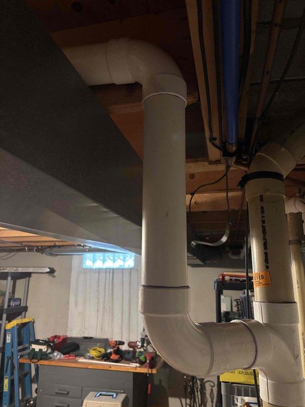 Completed installation of new kitchen drain line with connection to existing bathroom stack in basement area. Ran white PVC drainage pipe from kitchen location through floor joists, routing horizontally through ceiling structure before tying into vertical bathroom waste stack. Secured all piping with proper hangers and strapping per code requirements. Work included cutting and fitting PVC components, creating watertight connections, and ensuring proper slope for drainage. All exposed plumbing in unfinished basement area is properly supported and accessible for future maintenance. Installation completed with no obstructions to existing HVAC ductwork or other utilities.