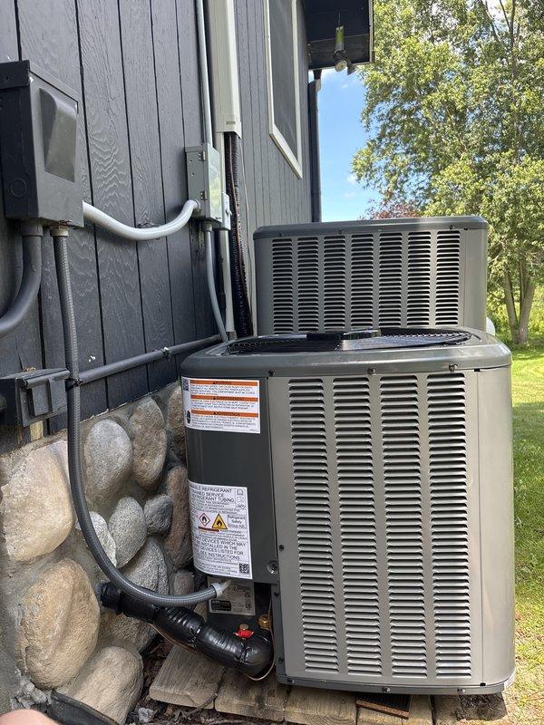 Completed full installation of new air conditioning system and air handler unit. Outdoor condensing unit positioned on concrete pad with proper refrigerant line routing and electrical conduit installation along exterior wall. System utilizes A2L refrigerant safety group compliant equipment with all service valves, connections, and manufacturer specifications properly configured and operational.