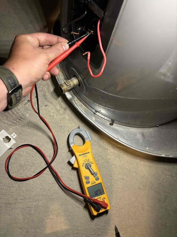 Responded to water heater issue on 4-year-old Rheem Professional unit with previous repair history. Performed electrical diagnostics using multimeter, testing voltage at heating element terminals (126V reading) and measuring amperage draw (12.1A reading) at blower motor assembly to verify proper operation. Completed system evaluation and discussed repair options versus replacement due to recurring problems with the unit.