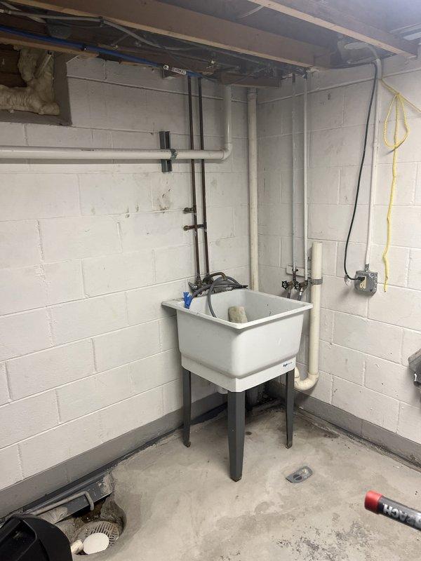 Completed rebuild of kitchen drain line in basement utility area. Installed new white PVC drainage piping running vertically along wall and connecting to existing plumbing infrastructure. Work included proper fitting connections, securing pipes to wall, and ensuring proper drainage flow to floor drain system.