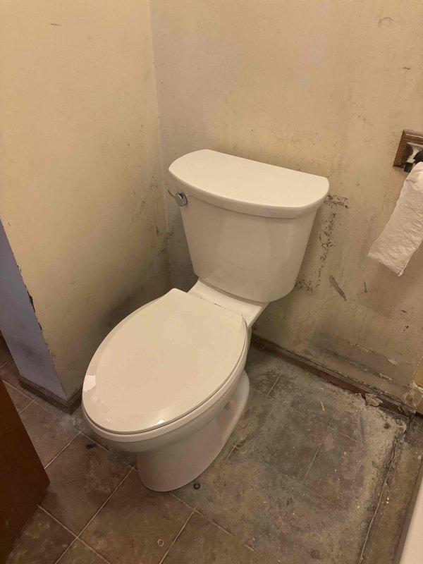 Completed installation of prefabricated white shower unit with integrated shelving, chrome grab bar, and flexible shower head assembly, including proper drain connection and threshold sealing. Installed new two-piece toilet with tank and bowl configuration, ensuring proper wax ring seal and water supply connection. Work performed in bathroom undergoing renovation with coordination around ongoing wall finishing and construction activities.