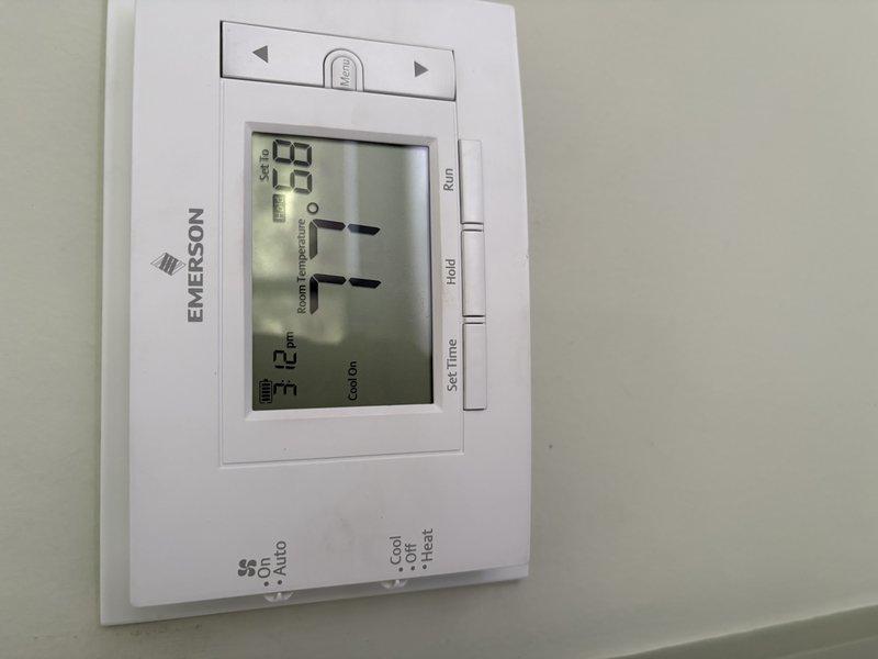 Responded to no cooling complaint on residential AC system. Upon arrival, verified thermostat was set to cooling mode and calling for cooling with indoor temperature reading 63°F. Inspected outdoor condenser unit and found significant rust corrosion on top panel indicating potential moisture intrusion or weathering damage. Evaluated system operation and determined unit was not achieving proper cooling performance. Documented equipment condition with photographs showing thermostat display and exterior condenser unit placement and condition for service records.