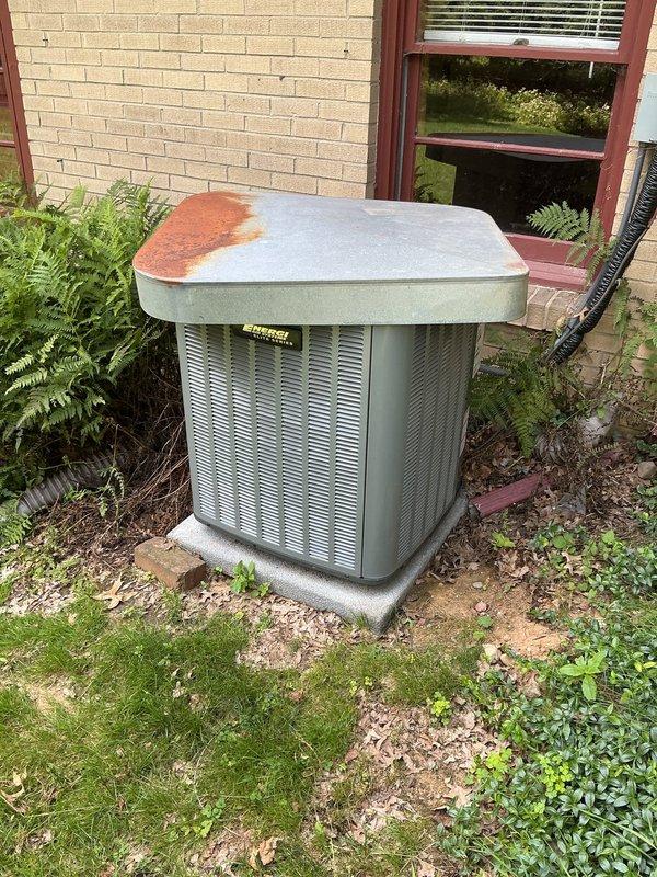 Responded to no cooling complaint on residential AC system. Upon arrival, verified thermostat was set to cooling mode and calling for cooling with indoor temperature reading 63°F. Inspected outdoor condenser unit and found significant rust corrosion on top panel indicating potential moisture intrusion or weathering damage. Evaluated system operation and determined unit was not achieving proper cooling performance. Documented equipment condition with photographs showing thermostat display and exterior condenser unit placement and condition for service records.