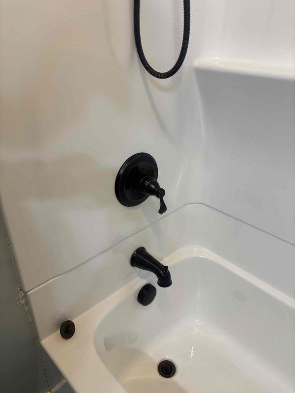 Responded to plumbing leak in main shower with malfunctioning faucet handle. Upon inspection, identified Delta brand shower fixture requiring attention. Assessed black-finished tub spout, single-handle faucet control, and handheld shower assembly mounted in white acrylic bathtub enclosure. Documented existing conditions showing water intrusion issue at shower valve assembly and compromised handle operation. Photographed fixture base components and overall installation to capture scope of repair needed for warranty claim processing through homeowner's coverage provider.