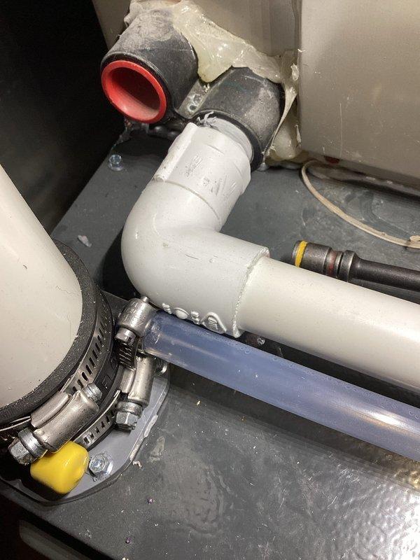 Completed annual cooling maintenance on 13-year-old air conditioning system. Performed comprehensive tune-up including inspection of all major components, refrigerant level check, electrical connections verification, condensate drain system evaluation, and filter assessment. Documented plumbing assembly and condensate drainage configuration with photographic evidence showing PVC drain lines, flexible tubing connections, and proper securing mechanisms with metal clamps in utility space.