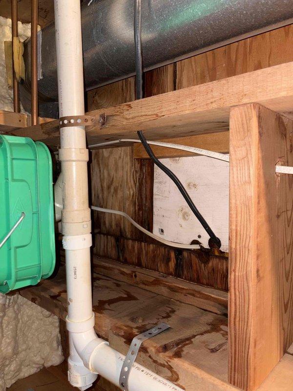 Responded to plumbing leak in basement of 1970s-era residential property where water was discovered on floor in rarely used room. Upon inspection, traced water source to leaking pipe connections in exposed basement plumbing system. Examined PVC drainage piping secured to wooden framing with metal strapping brackets and inspected under-sink cabinet plumbing including P-trap assembly, shut-off valves, and supply line connections. Documented conditions with photographs showing exposed framing, ductwork, and plumbing infrastructure in crawl space area, as well as cabinet interior with visible wear and moisture indicators. Confirmed leak location and provided assessment of aging plumbing system requiring repair to prevent further water damage.