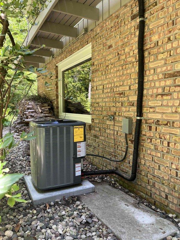 Complete residential HVAC system replacement performed, including outdoor condensing unit and indoor air handler installation. Removed existing equipment and installed new olive green outdoor unit on concrete pad against exterior brick wall. Mounted unit includes proper electrical disconnect box with black flexible conduit running vertically along wall for code-compliant power supply. Unit positioned in side yard utility area with appropriate clearances maintained.

Indoor air handler installed in attic space above existing Rheem Classic Plus Series 80 Two-Stage furnace. Connected refrigerant lines properly insulated and secured with mounting brackets. Integrated new air handler with existing galvanized ductwork system using proper elbow connections. All refrigerant lines charged and tested for proper operation. System startup completed with verification of cooling cycle, airflow, and thermostat communication. Installation meets manufacturer specifications and local building codes.