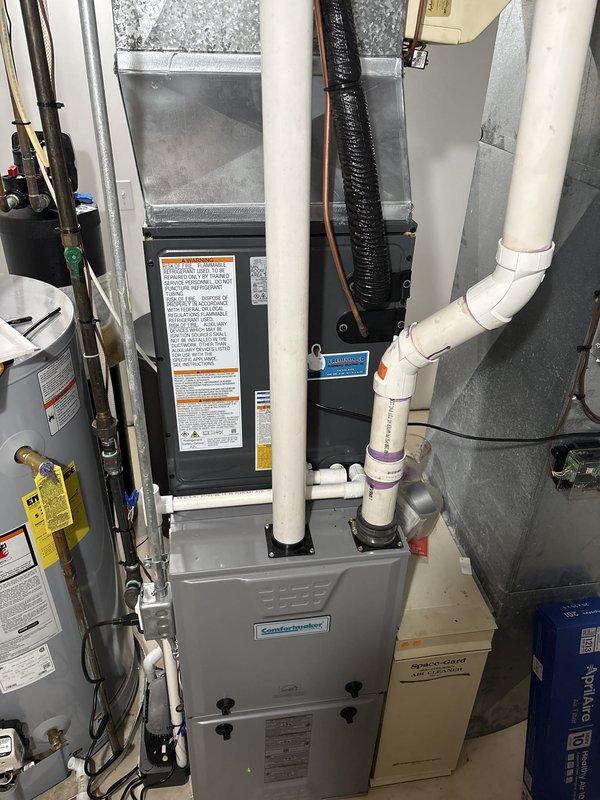 Complete HVAC system replacement performed at residential property. Removed existing air conditioning condenser unit and installed new outdoor condensing unit on concrete pad with proper stone base for drainage and stability. Unit positioned against exterior wall with adequate clearance for airflow and service access. Installed copper refrigerant line set and electrical disconnect box, securing all components to building exterior with appropriate mounting hardware.

Interior installation included new Comfortmaker furnace system in mechanical room, professionally mounted with proper clearances. Connected silver-gray supply and return ductwork to furnace plenum. Installed white PVC condensate drain lines and venting with proper primer application at all joints. Routed electrical conduit and refrigerant lines from outdoor condenser to indoor air handler. Verified all electrical connections at disconnect box and ensured proper voltage supply to equipment.

System startup procedures complet