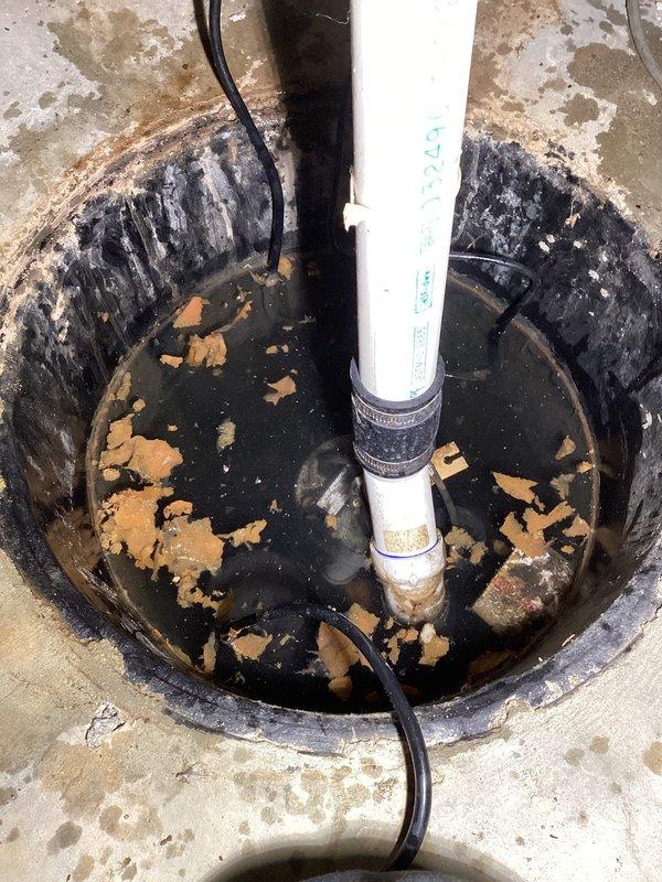 Responded to service call for orange-colored water in sump pump basin. Upon inspection, found severely corroded metal sump pit with extensive rust deterioration throughout interior walls, resulting in iron oxide contamination of standing water. Basin showed advanced corrosion with peeling, flaking rust and complete failure of protective coating on metal surfaces. Orange-brown rust debris and sediment observed floating on water surface. Documented existing conditions with photographs showing corroded pit, PVC discharge piping, pump electrical connections, and surrounding concrete floor with water staining.
