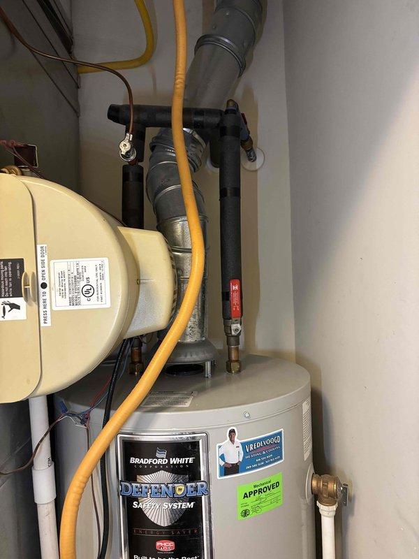 Responded to report of water collecting in drain pan under 5-year-old Bradford White water heater. Upon inspection, verified water heater installation and connections in residential utility closet. Documented equipment condition with photos showing Bradford White Defender Safety System model with standard plumbing connections, gas line, and HVAC equipment in confined space. All visible components including water lines, gas connections, and drain pan were assessed for proper operation and potential leak sources.