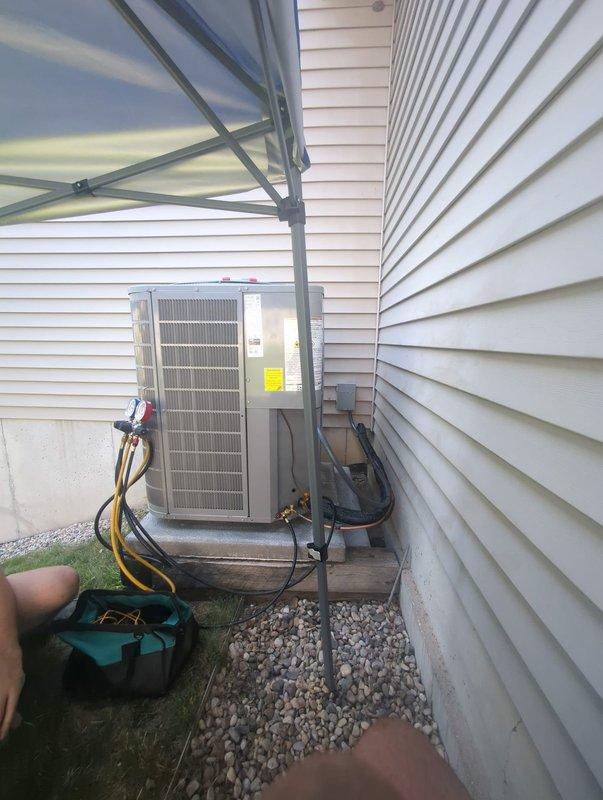 Completed full HVAC system installation including new furnace and air conditioning condenser unit. Outdoor AC unit positioned on concrete pad against building exterior with proper clearances maintained. Installed and secured refrigerant lines with insulation, routed along exterior wall using mounting brackets. Connected electrical wiring and service gauges for system startup and testing. Unit placed on gravel bed for drainage and leveling. System commissioned and verified operational parameters within manufacturer specifications.