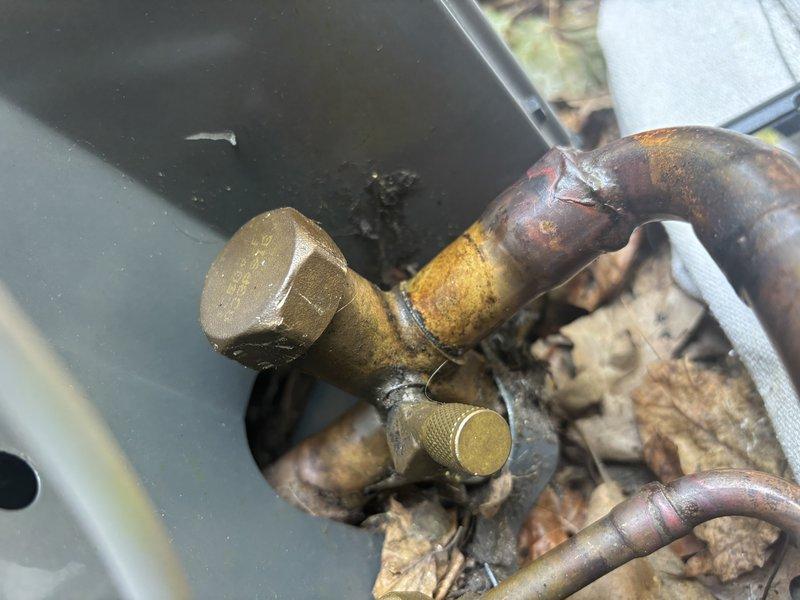 Performed refrigerant leak search on five-year-old AC system as recommended by prior technician. System currently cooling with no reported symptoms. Inspected evaporator coil connections and refrigerant lines, noting significant corrosion and oxidation on copper piping at valve junctions. No active refrigerant leaks detected during inspection. Documented condition of copper lines showing age-related deterioration for future reference.