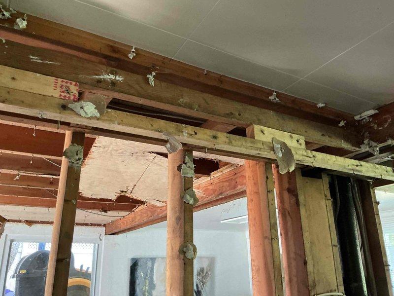 Responded to a drain problem in a 30-40 year old residential property where pipe replacement was required. Upon inspection, accessed the affected area through exposed floor joists and subflooring, revealing deteriorated wooden structural members with visible water damage, staining, and discoloration consistent with prolonged moisture exposure from the failing drain line. Documented extensive damage to ceiling framing and support beams, including evidence of previous water infiltration that had compromised the structural integrity of multiple joists. Photographed the existing conditions showing damaged lumber, metal joist hangers, and the routing of existing plumbing and electrical systems through the floor structure to provide comprehensive documentation for the necessary pipe replacement and potential structural repairs.
