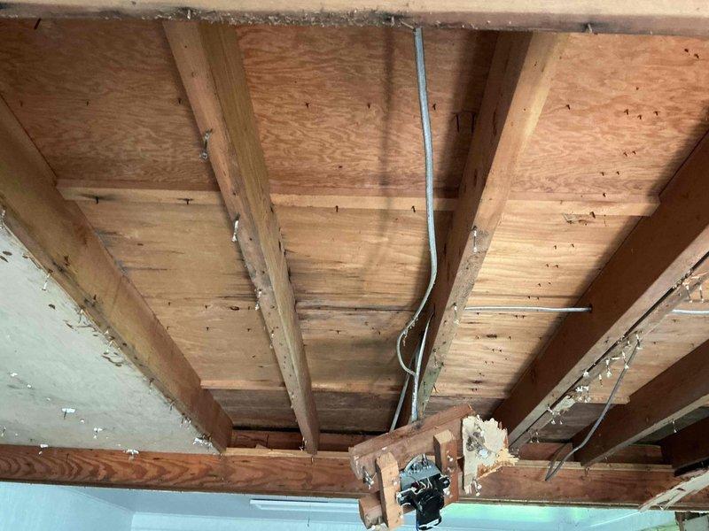 Responded to a drain problem in a 30-40 year old residential property where pipe replacement was required. Upon inspection, accessed the affected area through exposed floor joists and subflooring, revealing deteriorated wooden structural members with visible water damage, staining, and discoloration consistent with prolonged moisture exposure from the failing drain line. Documented extensive damage to ceiling framing and support beams, including evidence of previous water infiltration that had compromised the structural integrity of multiple joists. Photographed the existing conditions showing damaged lumber, metal joist hangers, and the routing of existing plumbing and electrical systems through the floor structure to provide comprehensive documentation for the necessary pipe replacement and potential structural repairs.