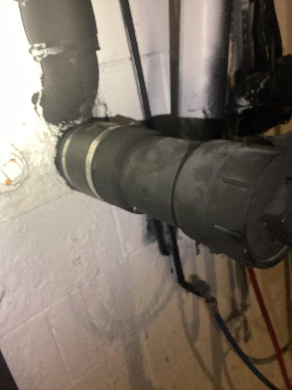 Responded to drain problem at property. Upon inspection, found corroded metal drain flange mounted to basement wall with significant rust buildup and mineral deposits obstructing the interior opening. Assessed plumbing assembly including vertical drain pipe connection showing signs of age, water damage, and debris accumulation around connection point. Documented existing conditions of wall-mounted drainage system and surrounding utility infrastructure for service records.