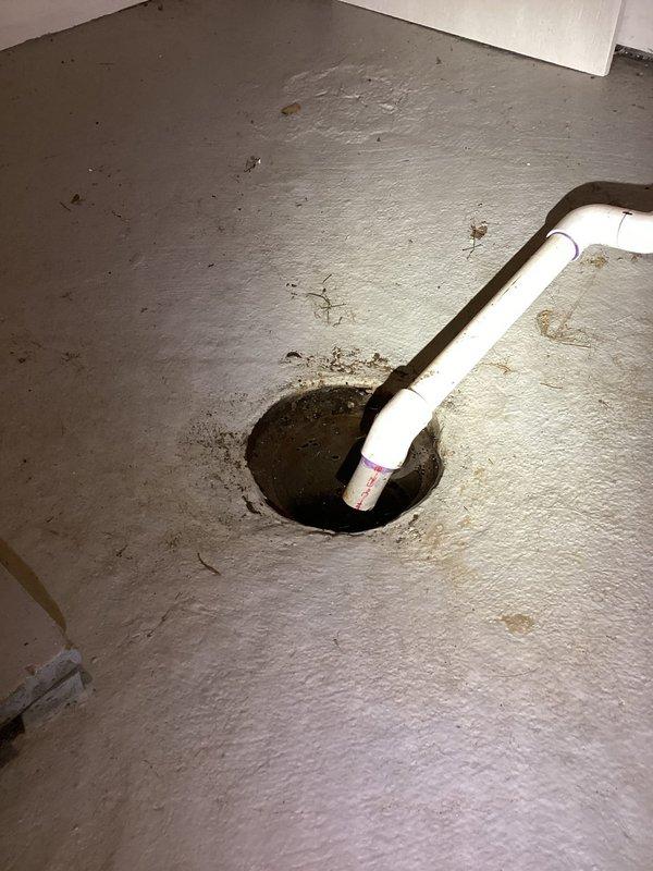 Inspected AC unit condensate drain line terminating at garage floor drain due to concerns about excessive condensation volume. Verified PVC drain pipe installation and confirmed proper drainage into floor drain with visible water staining around drain opening indicating active condensation discharge. System operating as designed with condensate properly routing to designated drain location.