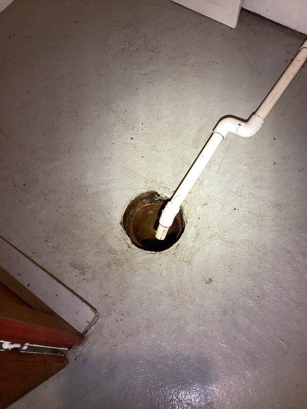 Inspected AC unit condensate drain line terminating at garage floor drain due to concerns about excessive condensation volume. Verified PVC drain pipe installation and confirmed proper drainage into floor drain with visible water staining around drain opening indicating active condensation discharge. System operating as designed with condensate properly routing to designated drain location.