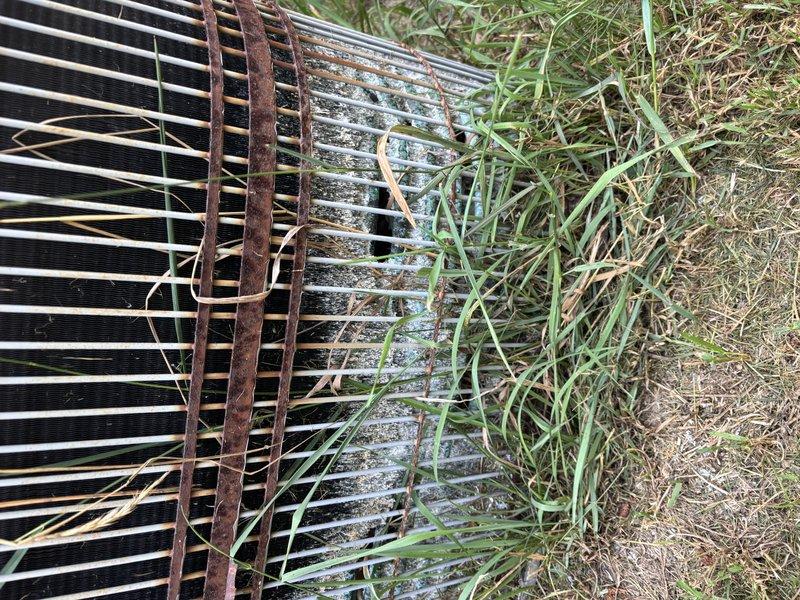 Completed annual cooling maintenance on 16-year-old air conditioning system. Performed comprehensive tune-up including inspection of condenser unit, which showed significant weathering, corrosion on frame components, and debris accumulation between coil fins. Cleaned condenser coils to remove dirt, organic matter, and vegetation growth that had reduced airflow efficiency. Addressed rust buildup on metal brackets and housing. System operational following service with improved heat exchange capability after coil cleaning and debris removal.