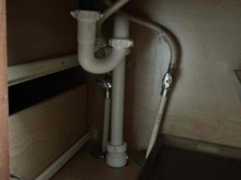 Completed comprehensive plumbing inspection of residential property including mechanical room and under-sink installations. Documented boiler system with copper supply piping, flexible venting connections, and associated HVAC ductwork in basement utility area. Inspected kitchen/bathroom sink drain assembly featuring standard P-trap configuration with PVC piping and braided supply lines, confirming proper installation and operational condition of all visible plumbing components.