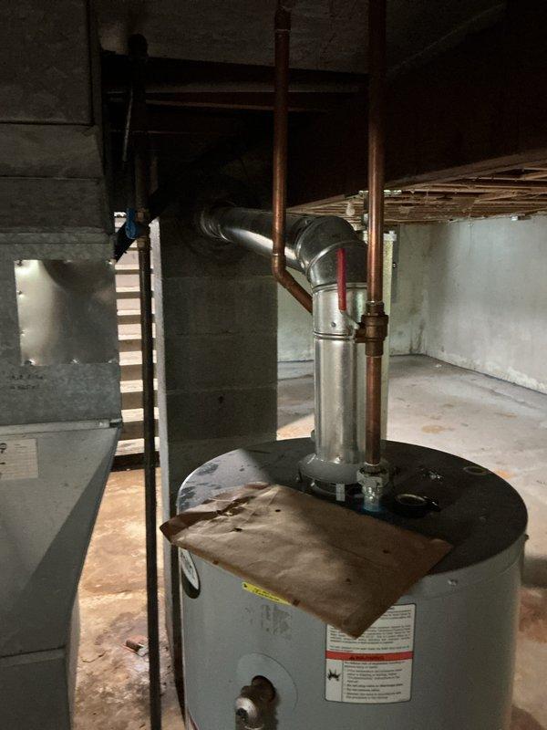 Responded to no hot water condition affecting entire residence. Upon inspection, found 11-year-old AO Smith water heater in basement utility area with significant dust accumulation and age-related wear. Unit located in unfinished basement space with proper venting through existing flue system connected to horizontal ductwork. Documented existing installation showing cylindrical tank-style heater with metallic flue pipe, red-handled valve connection, and manufacturer specification plate. Assessed basement infrastructure including concrete block walls, exposed floor joists, and concrete flooring suitable for replacement installation. Provided estimate for water heater replacement due to unit failure and age exceeding typical service life expectancy.