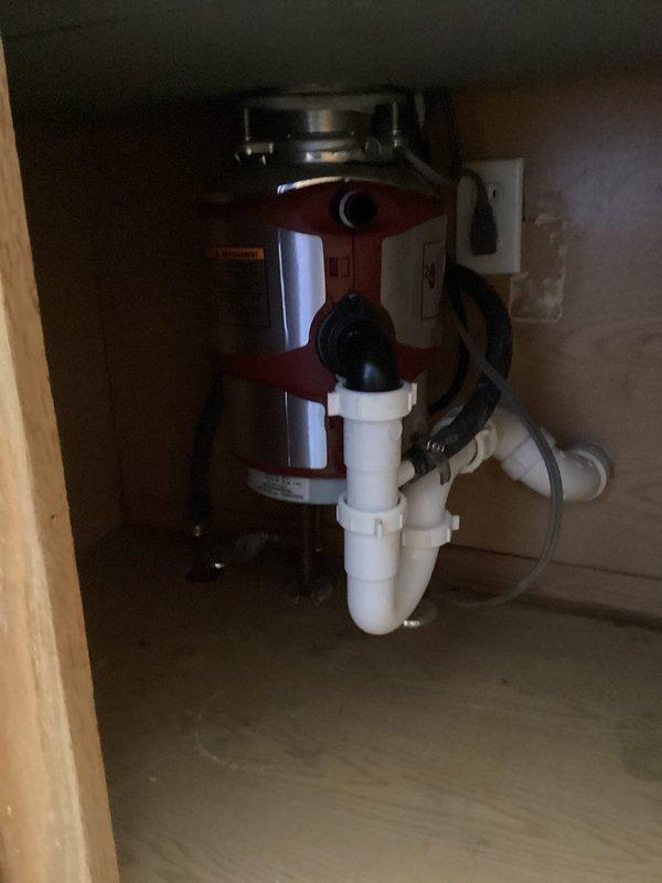 Completed new kitchen sink installation in residential property built in 1997. Installed stainless steel undermount basin with brushed nickel pull-down faucet and integrated garbage disposal unit with red cylindrical body. Connected disposal to drain system using white PVC P-trap configuration, verified all plumbing connections for proper drainage, and completed electrical hookup with standard plug connection to wall outlet. All fixtures tested and operational upon completion.