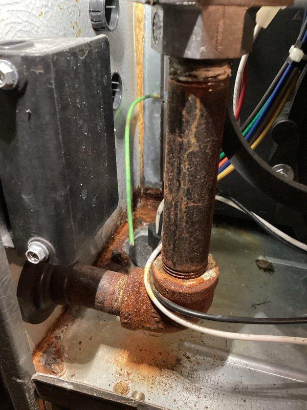 # ASTU-AC Super Tune-up Completed

Performed comprehensive super tune-up service on a 22-year-old air conditioning system located in a basement utility area with significant water damage and standing water present. The unit exhibited extensive corrosion on copper refrigerant lines, rusted pipe connections, and deteriorated metal components throughout, indicating prolonged moisture exposure. 

Conducted full system inspection despite challenging environmental conditions, including flooded workspace with murky standing water surrounding equipment. Examined motor assembly, electrical connections, and wiring harnesses which showed signs of age but remained functional. Documented heavily corroded copper elbow joints and pipe connections with reddish-brown oxidation, along with rust-stained condensate pan and metal framework.

Inspected all electrical components including multi-colored wire bundles, ground wire connections, and control box housing. Verified proper wire routing and connection