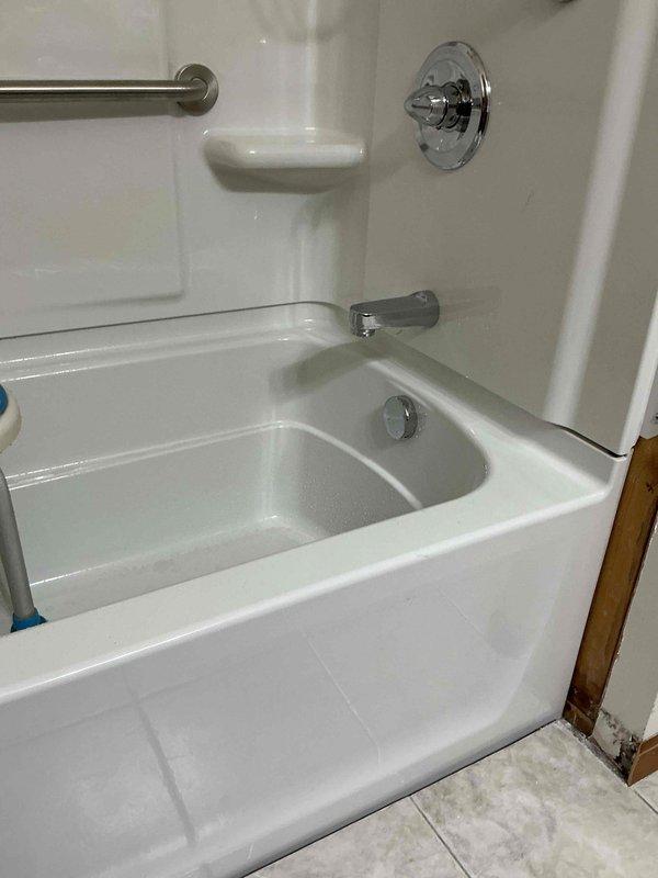 Completed full bathtub and shower surround replacement with new faucet installation over a two-day period. Removed existing tub/shower unit and installed new white fiberglass shower surround system with integrated corner shelving, recessed soap dish, and textured wall panels. Installed new chrome shower valve with circular trim plate, tub spout, and mounted stainless steel grab bar on back wall for safety compliance. All plumbing connections tested and verified leak-free, with completed installation meeting current building codes.