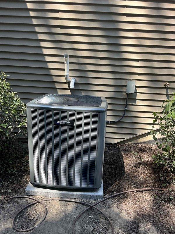 Completed full HVAC system installation including outdoor condensing unit and indoor air handler. Outdoor unit installed on composite pad with proper electrical conduit routing, PVC condensate drain line, and refrigerant line connections. Indoor Goodman air handler installed in basement mechanical room with integrated ductwork connections, electrical service, and proper clearances maintained around existing water heater and utility equipment.