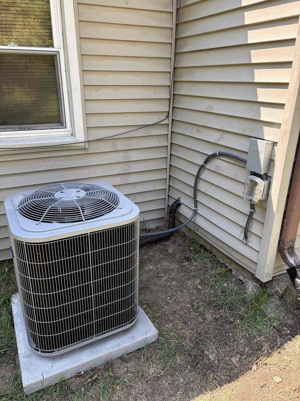 Successfully completed full HVAC system replacement including new Carrier furnace and outdoor condensing unit. Installed furnace in basement mechanical room with complete ductwork assembly, including metallic supply plenum and curved elbow transitions. Mounted new white cylindrical AC condenser on existing concrete pad against exterior wall with proper refrigerant line routing through wall penetration and secure electrical connections via exterior junction box. All components tested and operational upon completion.