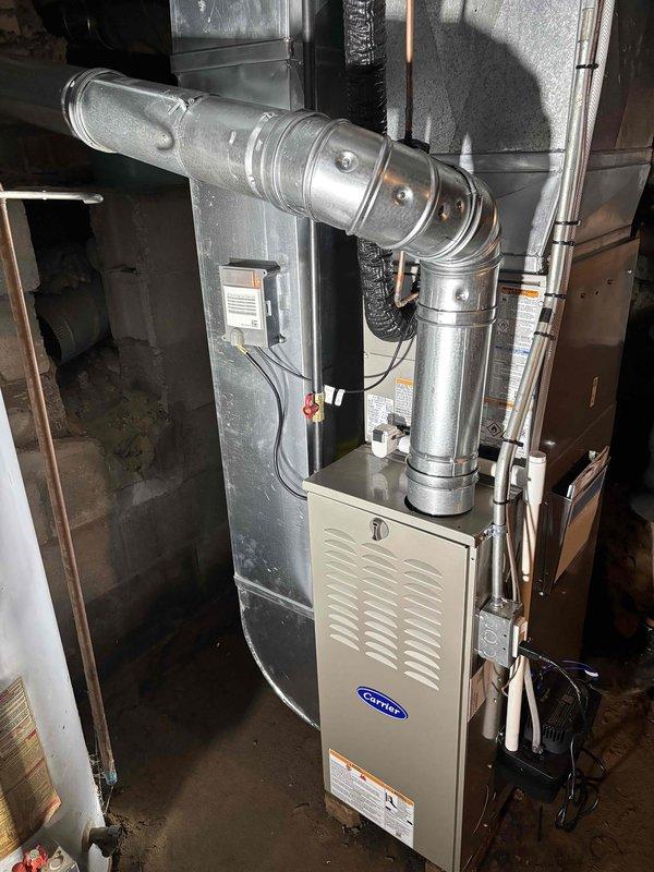 Successfully completed full HVAC system replacement including new Carrier furnace and outdoor condensing unit. Installed furnace in basement mechanical room with complete ductwork assembly, including metallic supply plenum and curved elbow transitions. Mounted new white cylindrical AC condenser on existing concrete pad against exterior wall with proper refrigerant line routing through wall penetration and secure electrical connections via exterior junction box. All components tested and operational upon completion.