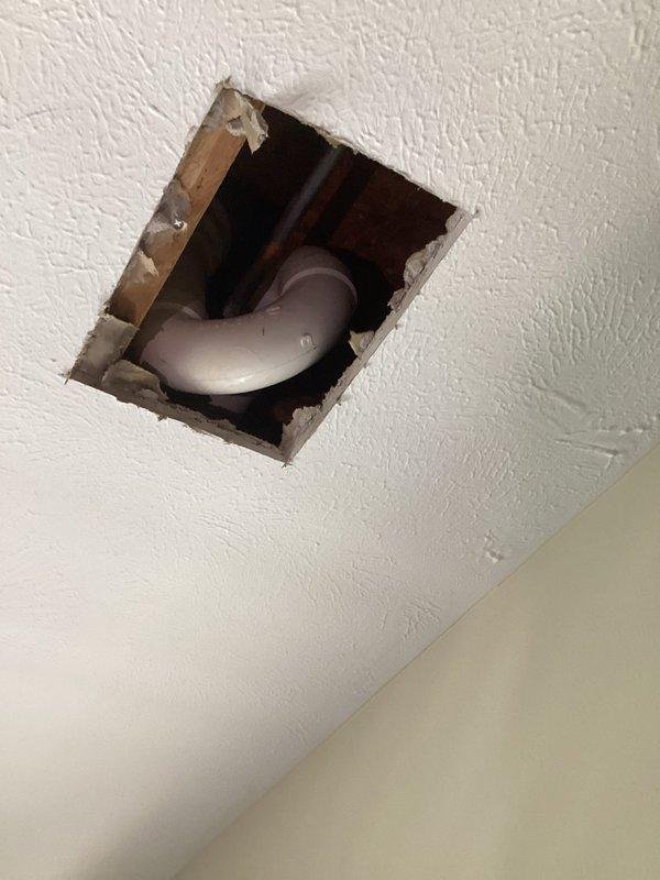 Responded to emergency plumbing leak originating from bathroom shower with active water intrusion affecting dining room ceiling below. Upon arrival, identified visible water damage to ceiling with soft, saturated drywall and discoloration indicating ongoing leak. Created access opening in affected ceiling area to locate source of water infiltration. Inspection revealed compromised PVC plumbing connection in shower drain assembly above damaged ceiling. Documented existing conditions including water-stained textured ceiling surface and exposed plumbing infrastructure for assessment and repair planning.