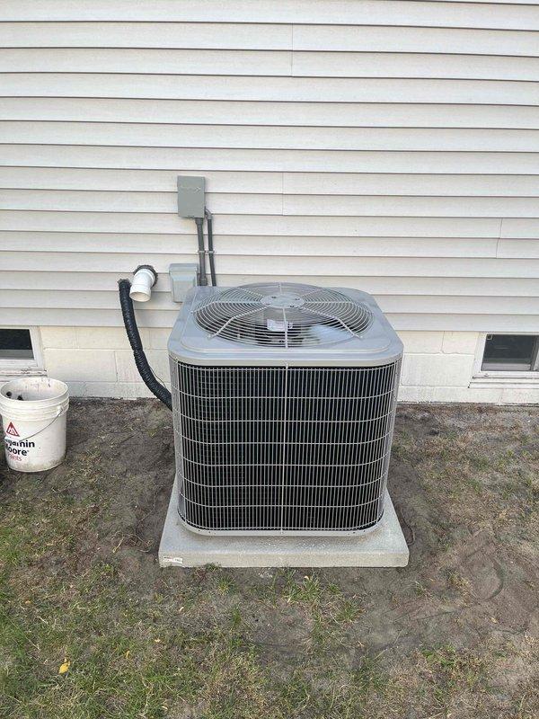 Completed full air conditioning system replacement including outdoor condenser unit and indoor air handler components. Installed new Goodman brand furnace with integrated cooling system in basement utility area, routing white PVC condensate drainage and exhaust venting with proper 90-degree fittings. Mounted outdoor condenser unit on concrete pad against building exterior with appropriate clearances, connected refrigerant lines via insulated line set, and ran black flexible electrical conduit to power supply with wall-mounted disconnect box. Secured all ductwork connections including metallic flex duct for proper air distribution, verified all electrical connections meet code requirements, and ensured system is operational and ready for use.