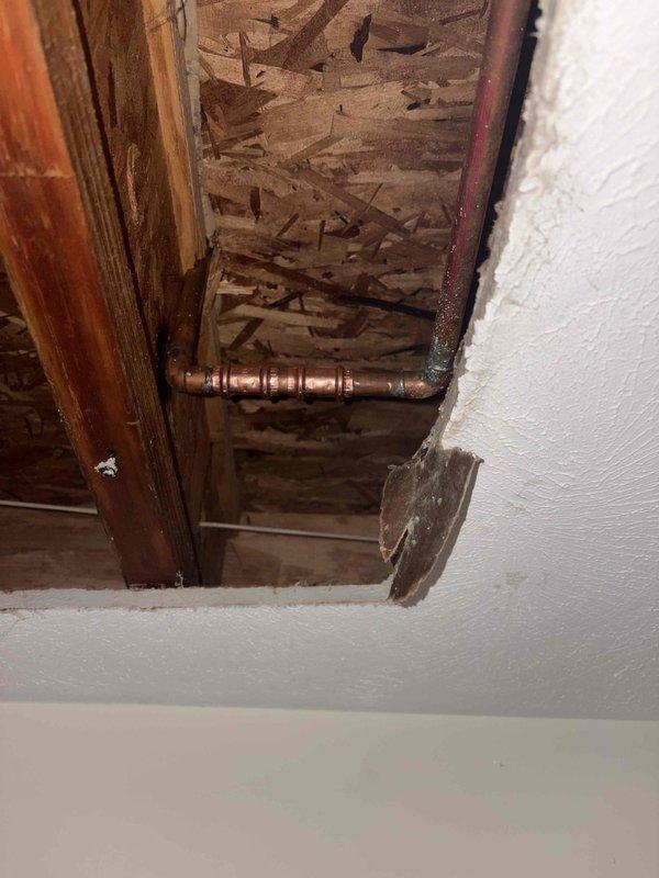 Responded to emergency call for water leaking through ceiling from unknown source. Instructed client to locate and close main water shut-off valve to prevent further water damage. Investigated leak source by accessing crawl space and ceiling cavity, where copper supply piping was found with significant condensation and active moisture accumulation on pipe surfaces and joints. Documented conditions with photos showing wet copper piping with elbow connections in crawl space area and ceiling access point exposing affected plumbing system. Provided immediate guidance on emergency water shut-off procedures to minimize property damage until repairs could be completed.