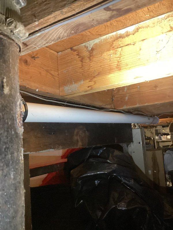Responded to emergency plumbing leak under kitchen sink with active water flow. Upon inspection, traced leak source to deteriorated pipe connection in crawl space beneath kitchen area. Found severely corroded joint between dissimilar metal pipes with extensive white mineral deposits and crystallization indicating prolonged water seepage. Upper pipe showed significant paint deterioration and surface degradation, while copper lower pipe exhibited green oxidation and patina buildup. Replaced failed connection point, secured proper pipe support along wooden joists, and installed black plastic sheeting for moisture protection. Verified all connections were watertight, tested water flow throughout system, and confirmed no additional leaks in surrounding areas. Documented conditions with photos for record. System restored to full operation with no further water discharge detected.
