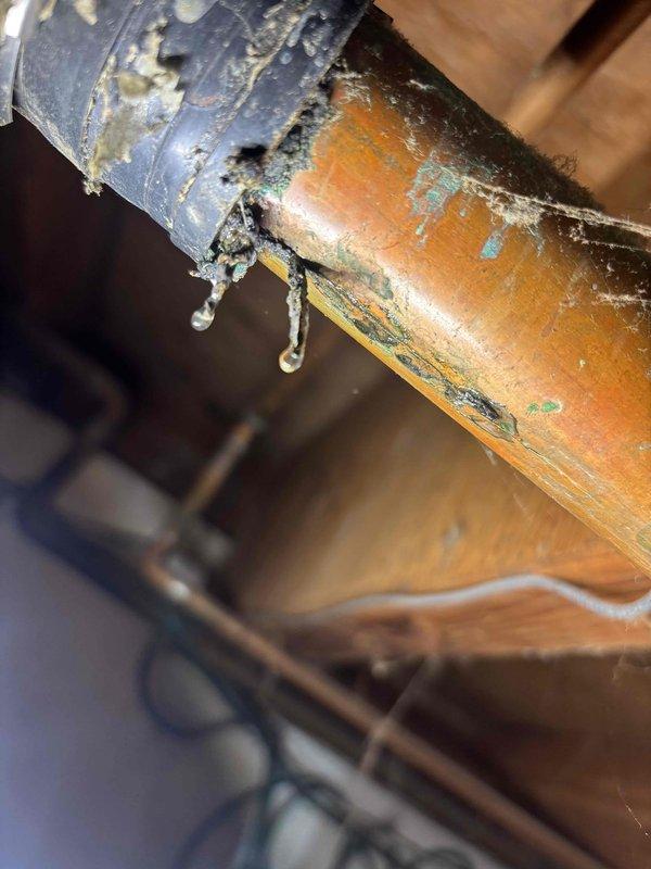 Responded to emergency plumbing leak under kitchen sink with active water flow. Upon inspection, traced leak source to deteriorated pipe connection in crawl space beneath kitchen area. Found severely corroded joint between dissimilar metal pipes with extensive white mineral deposits and crystallization indicating prolonged water seepage. Upper pipe showed significant paint deterioration and surface degradation, while copper lower pipe exhibited green oxidation and patina buildup. Replaced failed connection point, secured proper pipe support along wooden joists, and installed black plastic sheeting for moisture protection. Verified all connections were watertight, tested water flow throughout system, and confirmed no additional leaks in surrounding areas. Documented conditions with photos for record. System restored to full operation with no further water discharge detected.