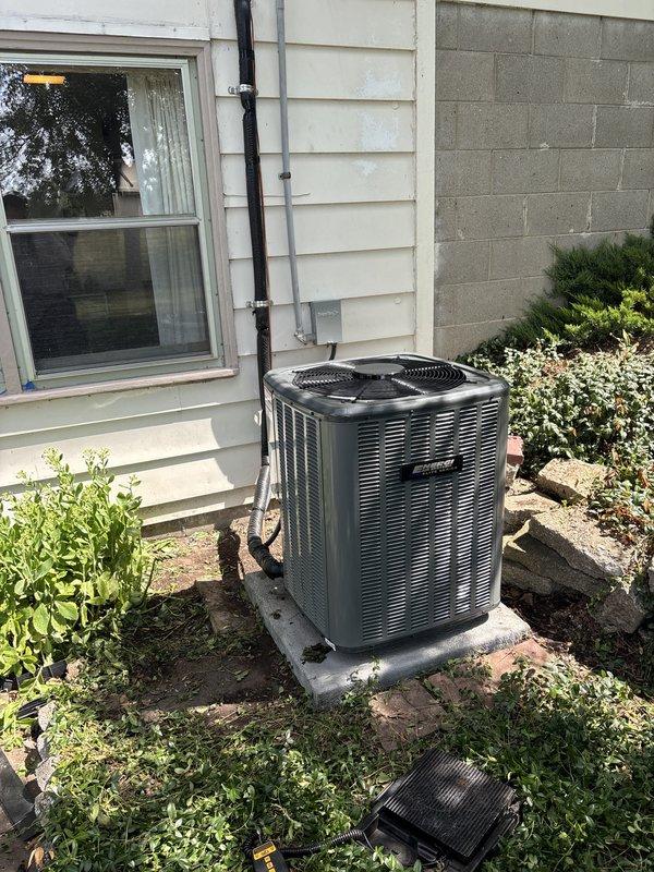 Completed full HVAC system installation including outdoor condenser unit and indoor air handler. Installed new condenser on concrete pad against exterior wall with proper refrigerant line routing and electrical conduit secured to siding. Connected indoor air handler to existing furnace in basement mechanical room with new supply ductwork and flexible coupling. Verified all electrical connections, refrigerant lines, and condensate drainage. System tested and operational.