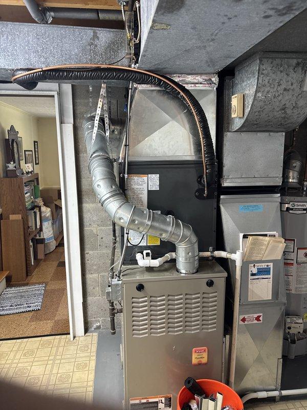 Completed full HVAC system installation including outdoor condenser unit and indoor air handler. Installed new condenser on concrete pad against exterior wall with proper refrigerant line routing and electrical conduit secured to siding. Connected indoor air handler to existing furnace in basement mechanical room with new supply ductwork and flexible coupling. Verified all electrical connections, refrigerant lines, and condensate drainage. System tested and operational.