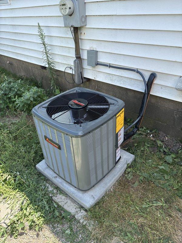 Completed full HVAC system installation including new furnace and air conditioning condenser unit. Installed furnace on protective platform in basement utility area with proper venting via white PVC piping and connected black flexible ductwork. Mounted outdoor AC condenser unit on concrete pad adjacent to building exterior with electrical conduit and refrigerant lines properly routed up vinyl siding to connection point near electric meter. All equipment installed per manufacturer specifications with appropriate labeling intact, system commissioned and operational.