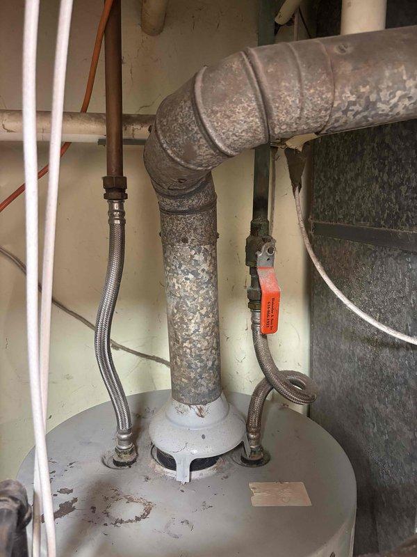 Responded to no cooling call on five-year-old residential air conditioning system affecting entire home. Upon arrival, performed diagnostic assessment of HVAC equipment located in utility closet adjacent to water heater. Inspected air handler unit and associated ductwork in basement area, noting significant deterioration of metal ductwork with visible corrosion and flaking surface finish on 90-degree elbow joint and connected sections. Evaluated mechanical connections, electrical supply, and refrigerant lines to air handler. Documented equipment condition through photographs showing HVAC unit positioning, plumbing connections, and compromised ductwork requiring attention for proper system airflow and efficiency.