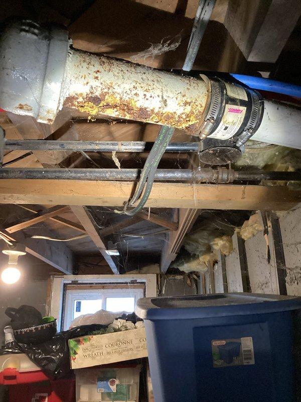 Completed kitchen drain repair in basement area. Addressed severely corroded white PVC drain piping showing extensive rust-colored deterioration and replaced damaged sections. Repaired structural support column exhibiting significant rust damage and corrosion at lower sections to ensure proper drainage system integrity.