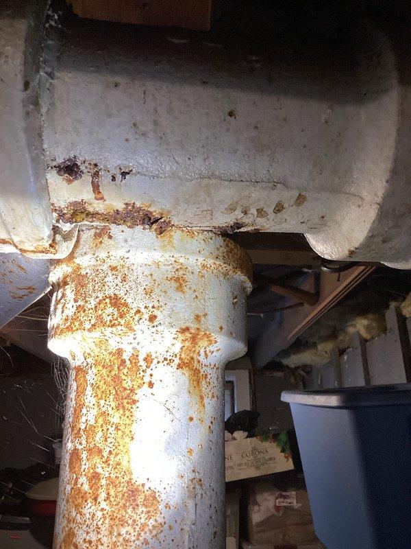 Completed kitchen drain repair in basement area. Addressed severely corroded white PVC drain piping showing extensive rust-colored deterioration and replaced damaged sections. Repaired structural support column exhibiting significant rust damage and corrosion at lower sections to ensure proper drainage system integrity.